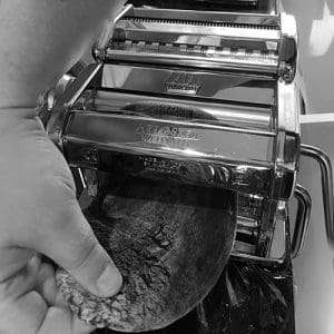 Cuttlefish Ink Fettuccine pasta dough being fed through pasta machine