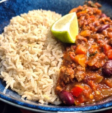 Chilli con carne with brown rice and wedge of lime.