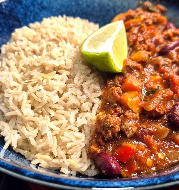 Chilli con carne with brown rice and wedge of lime.